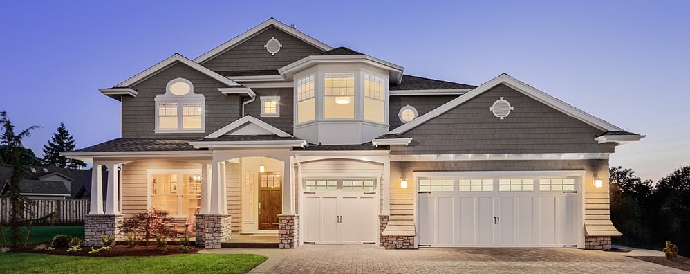 An elegant white house with garage and house lights on at dusk