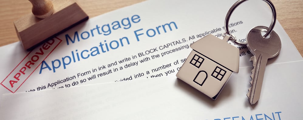 Key with house keychain placed on top of a mortgage application with APPROVED stamp