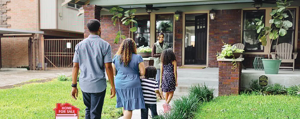 Family approaches a house with "Home for Sale" sign as a person with clipboard welcomes them.