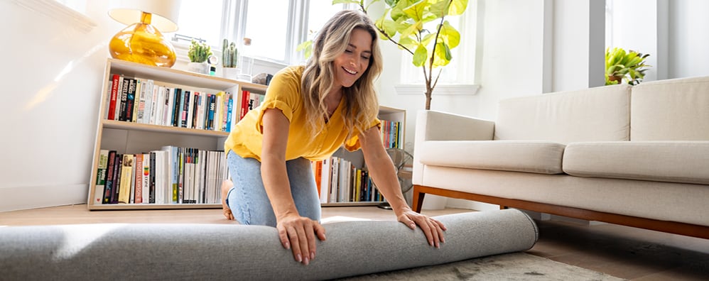 Happy woman moving house and unrolling a carpet while unpacking