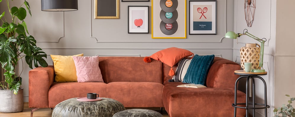 Eclectic living room with a rust-colored sofa adorned with colorful pillows and a throw. Walls showcase diverse framed art, with a cozy, vibrant ambiance.
