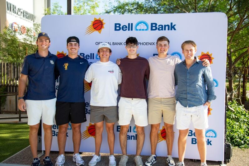 A group of men standing in front of the Bell Bank Collegiate backdrop