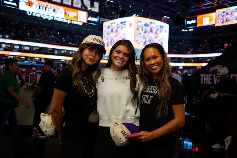 Three people smiling with a stadium in the background