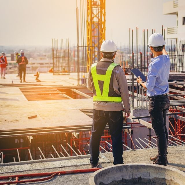 A construction worker and a professional in a dress shirt, both in hard hats, gesturing at a construction site.