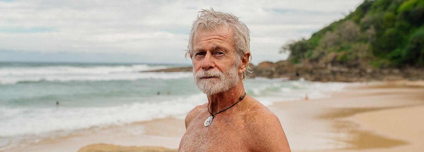 a photo of man with grey hair and a short grey beard standing at the beach