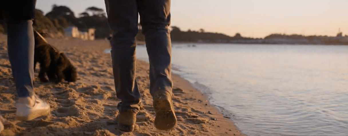 Two people walking along a shore at sunset.