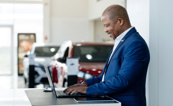 Employee in blue suit at high-end car dealership reviewing a laptop. 