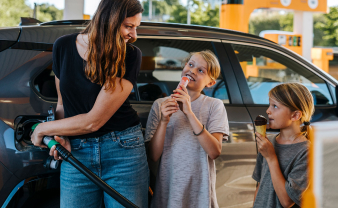 Mom putting gas in her car with her kids smiling and holding snacks. 