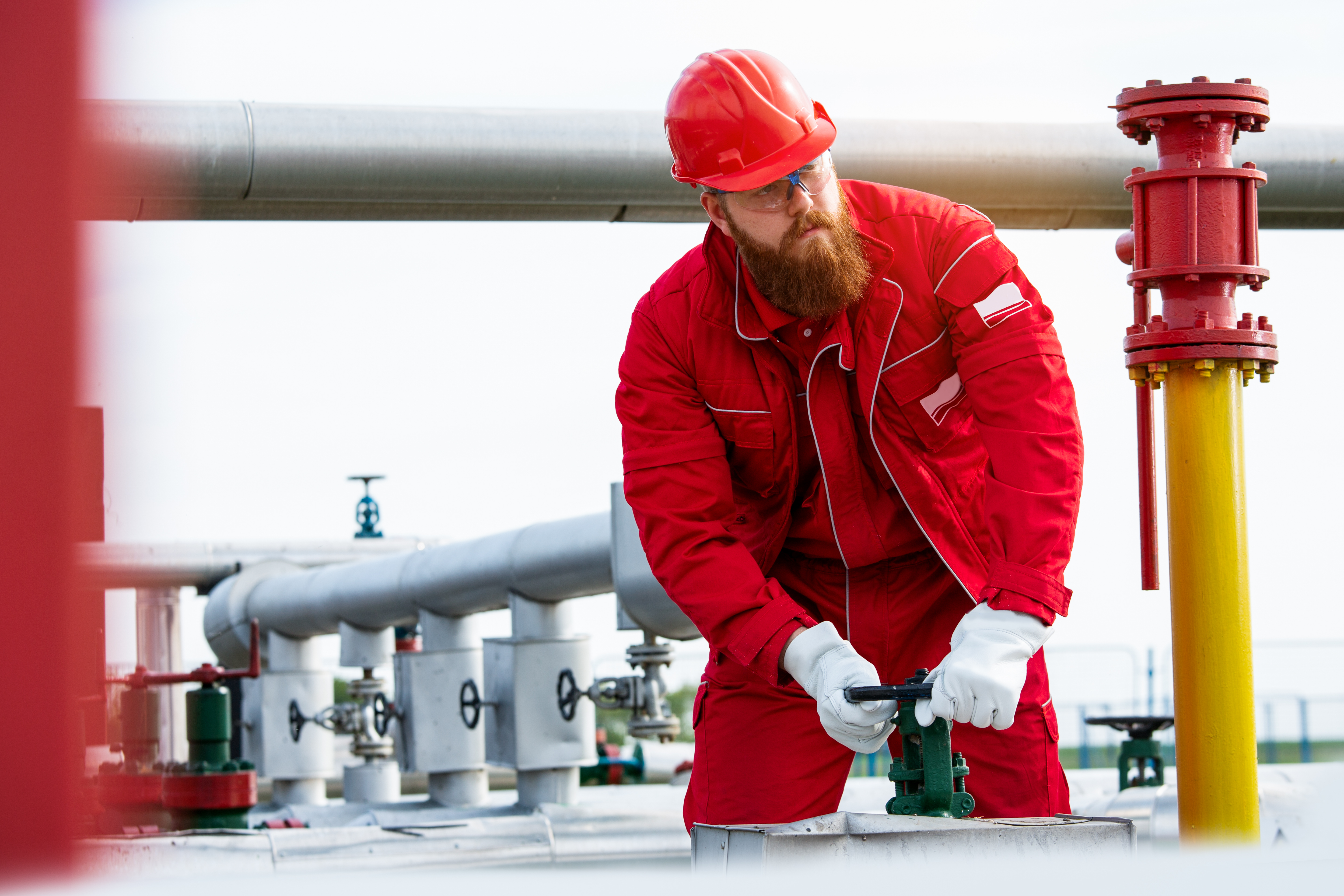 Energy worker in red construction suit and hard hat turning a valve.