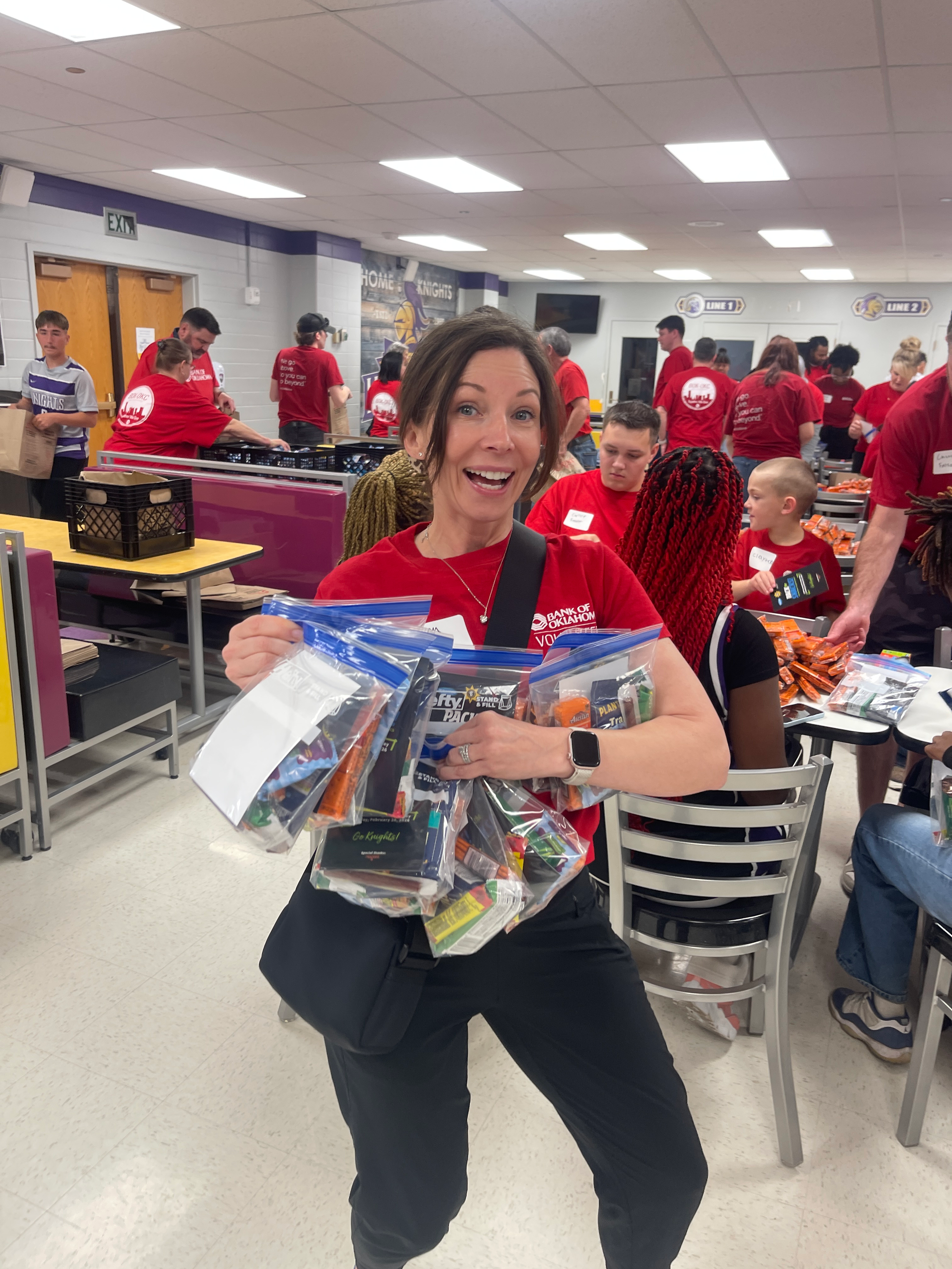 Bank of Oklahoma volunteer poses while holding snacks for Pack the Snacks NW Classen.