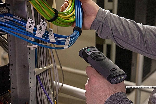 A data center technician uses a barcode scanner to identify server rack cables.