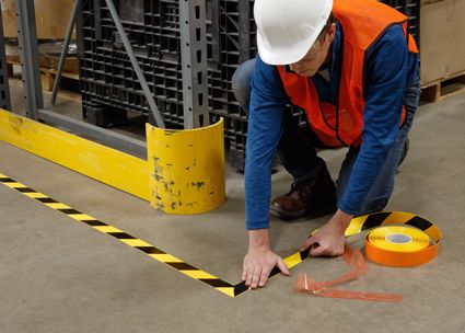 Worker in hardhat applies Brady Toughstripe yellow and black tape to floor.