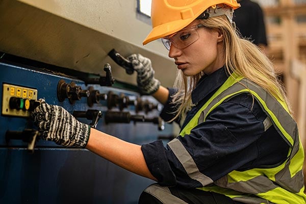 Worker in safety gear operates panels on a large machine. 