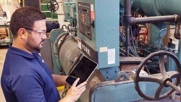 A man with a tablet inspects industrial machinery.
