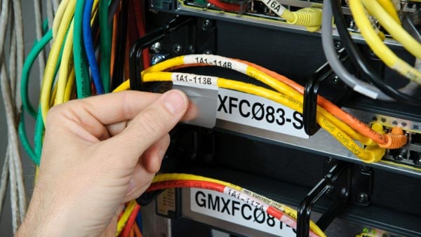 A hand attaching a self-laminating datacom wire label in a server rack.