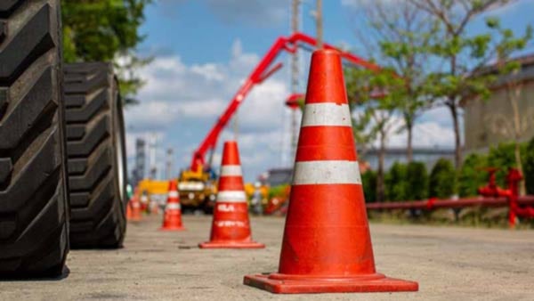 Orange and white traffic cone next to construction equipment on the road.