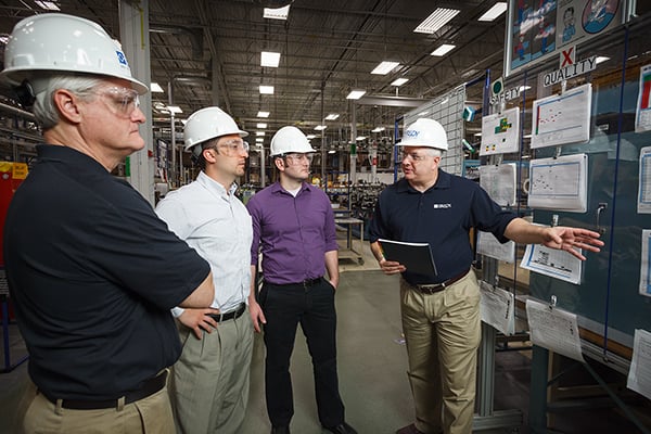 Four employees in hard hats review a Lean Daily Management board.