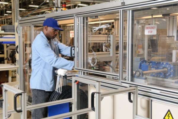 Employee in a blue shirt and blue cap operating industrial machinery.