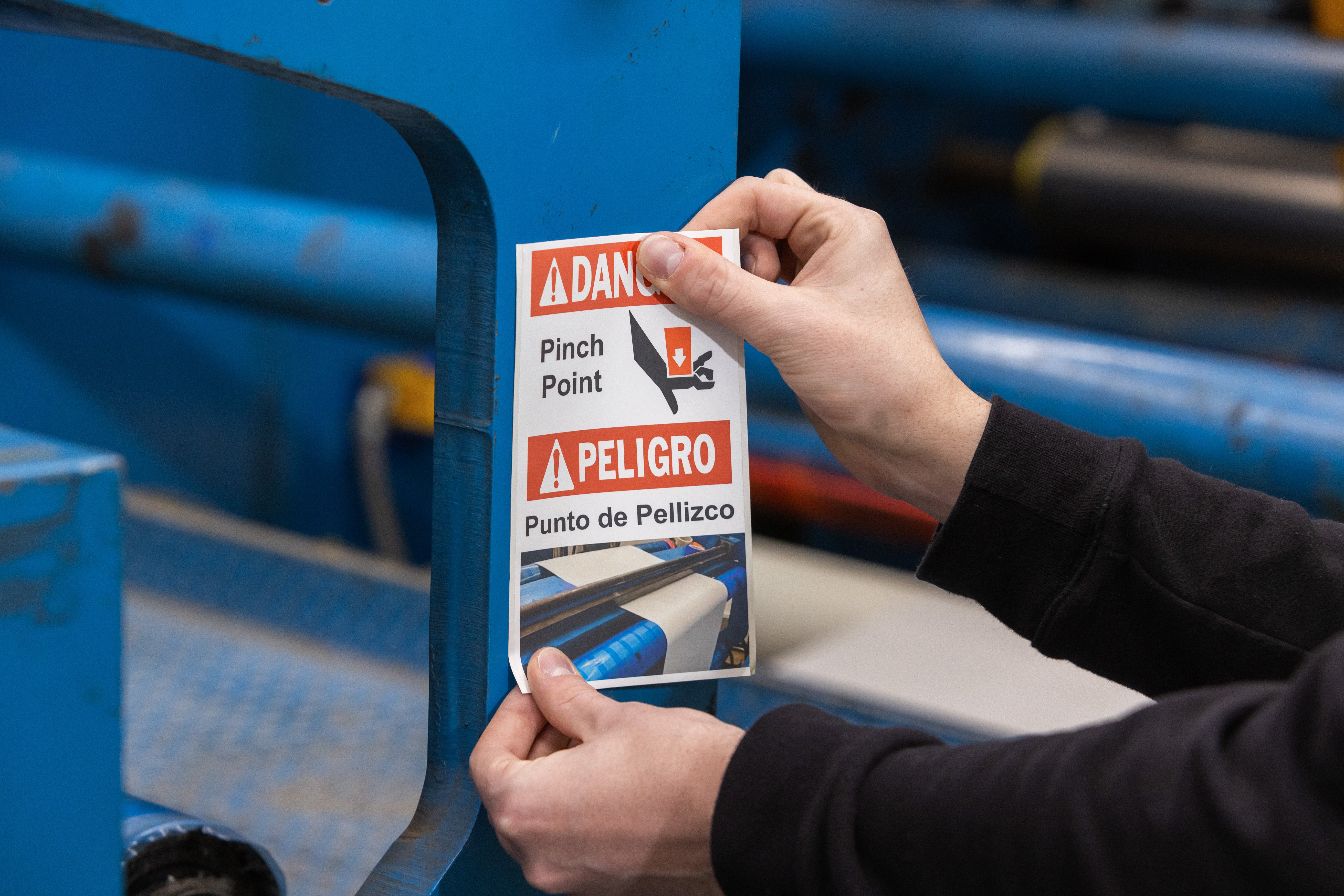 Person applying a pinch point warning label to a manufacturing machine.