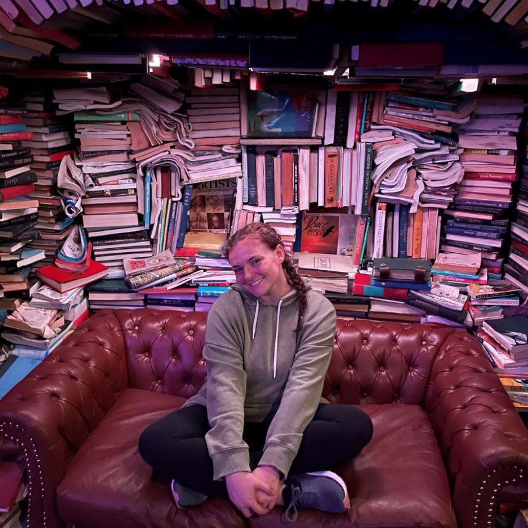 Brunel Account Coordinator Katie Rossman sits on a couch in front of a library of stacked books