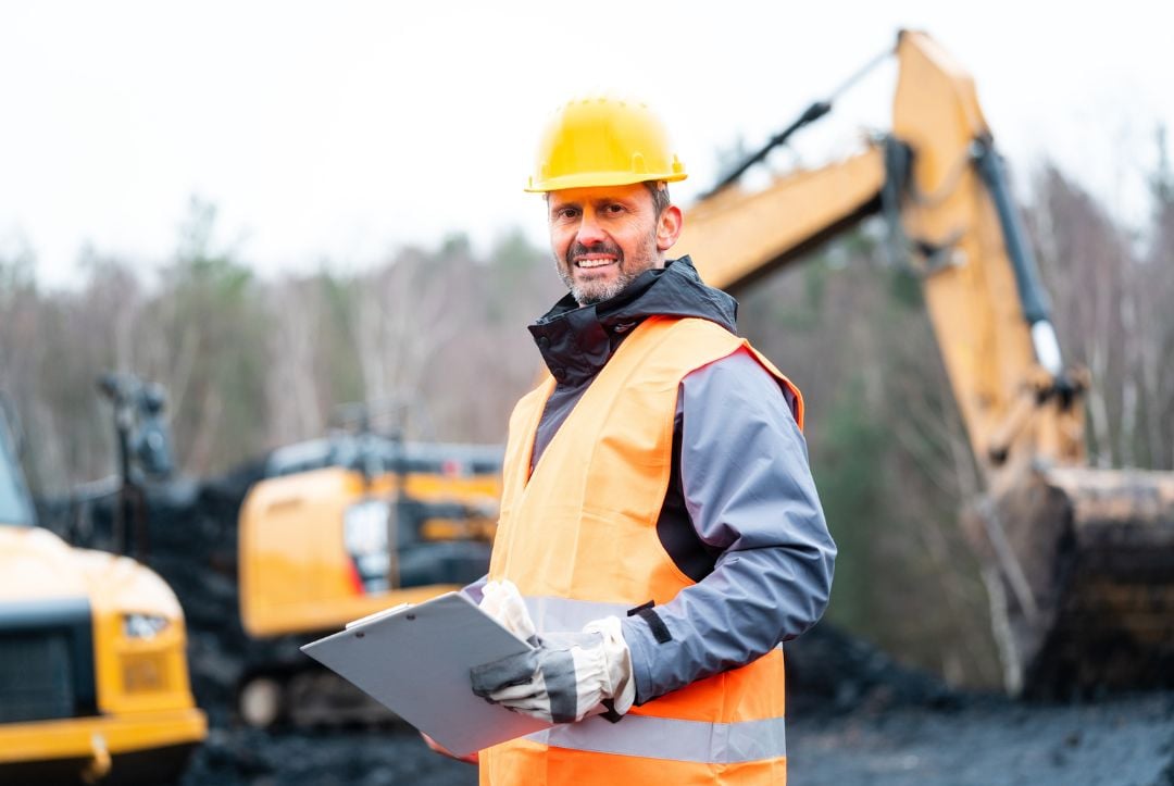 Heavy Equipment Operator smiling in front of an excavator.