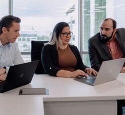 Project manager and 2 men meet in conference room in front of laptops