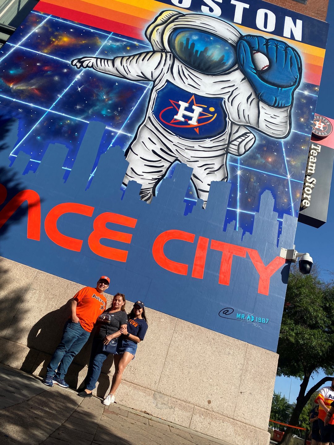 Family of 3 poses in front of a large Houston Astros mural in downtown Houston that reads "Space City"