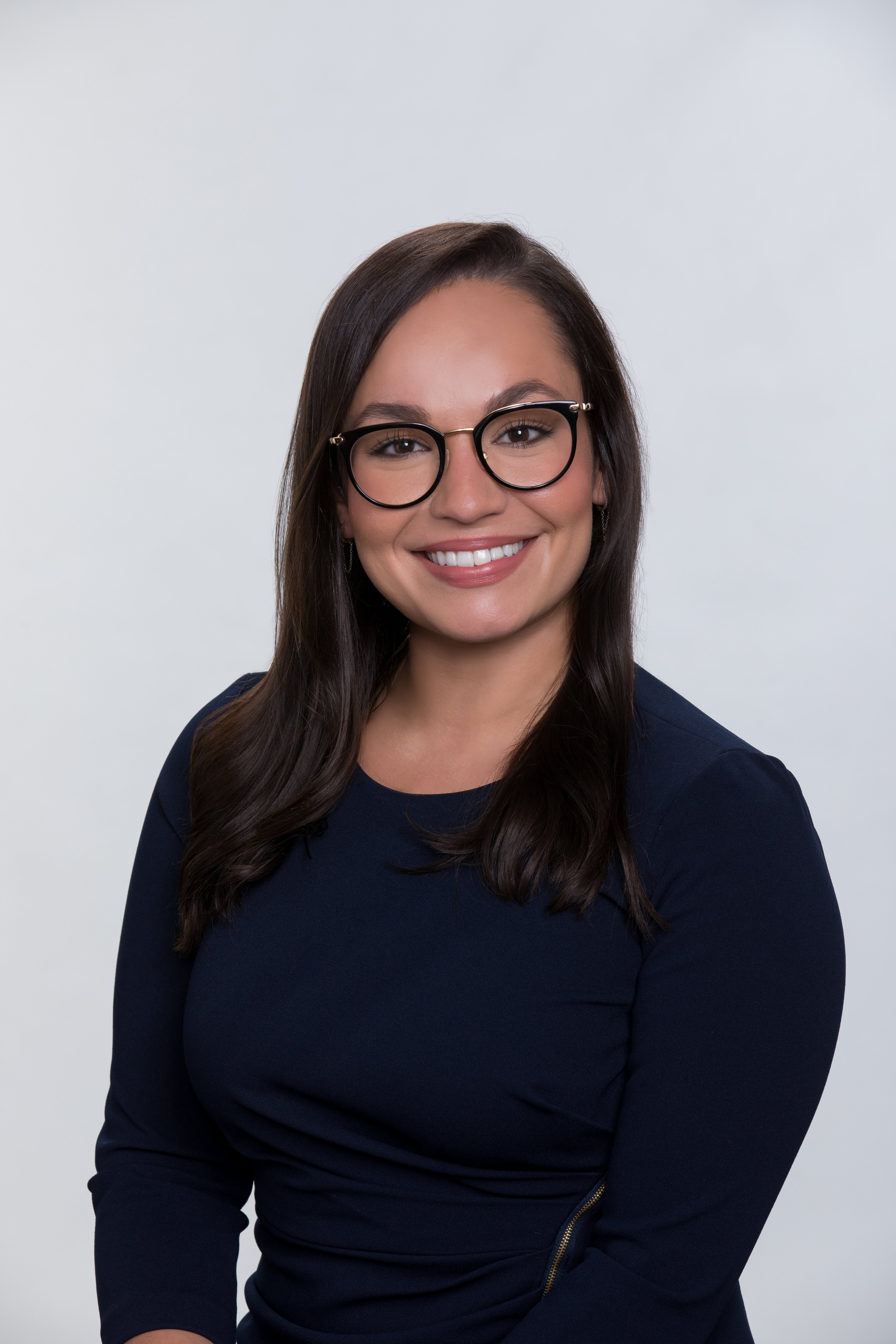 Professional headshot of woman with brunette hair, large glasses, and a black long-sleeve top