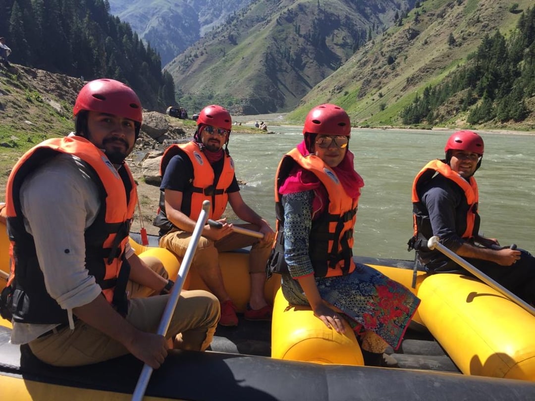 3 men and 1 woman in yellow boat wearing orange life jackets and red helmets