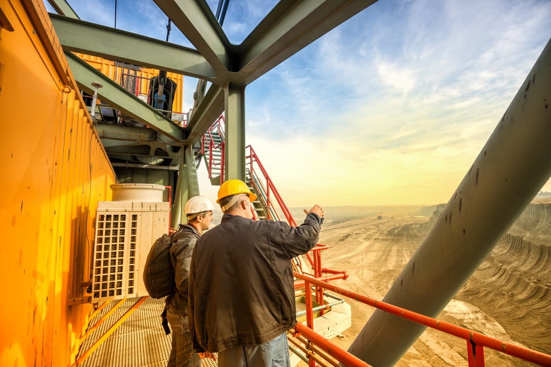 2 men in hard hats looking over mine from above