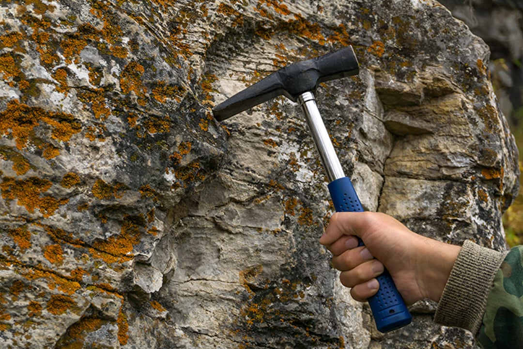 Geologist's hand strikes a rock with a hammer to take a sample