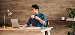 Man at desk drinking coffee and working on his laptop