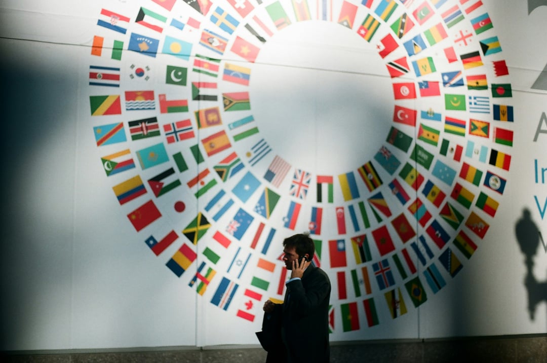 A man talking on the phone with a backdrop of international country flags in the background.