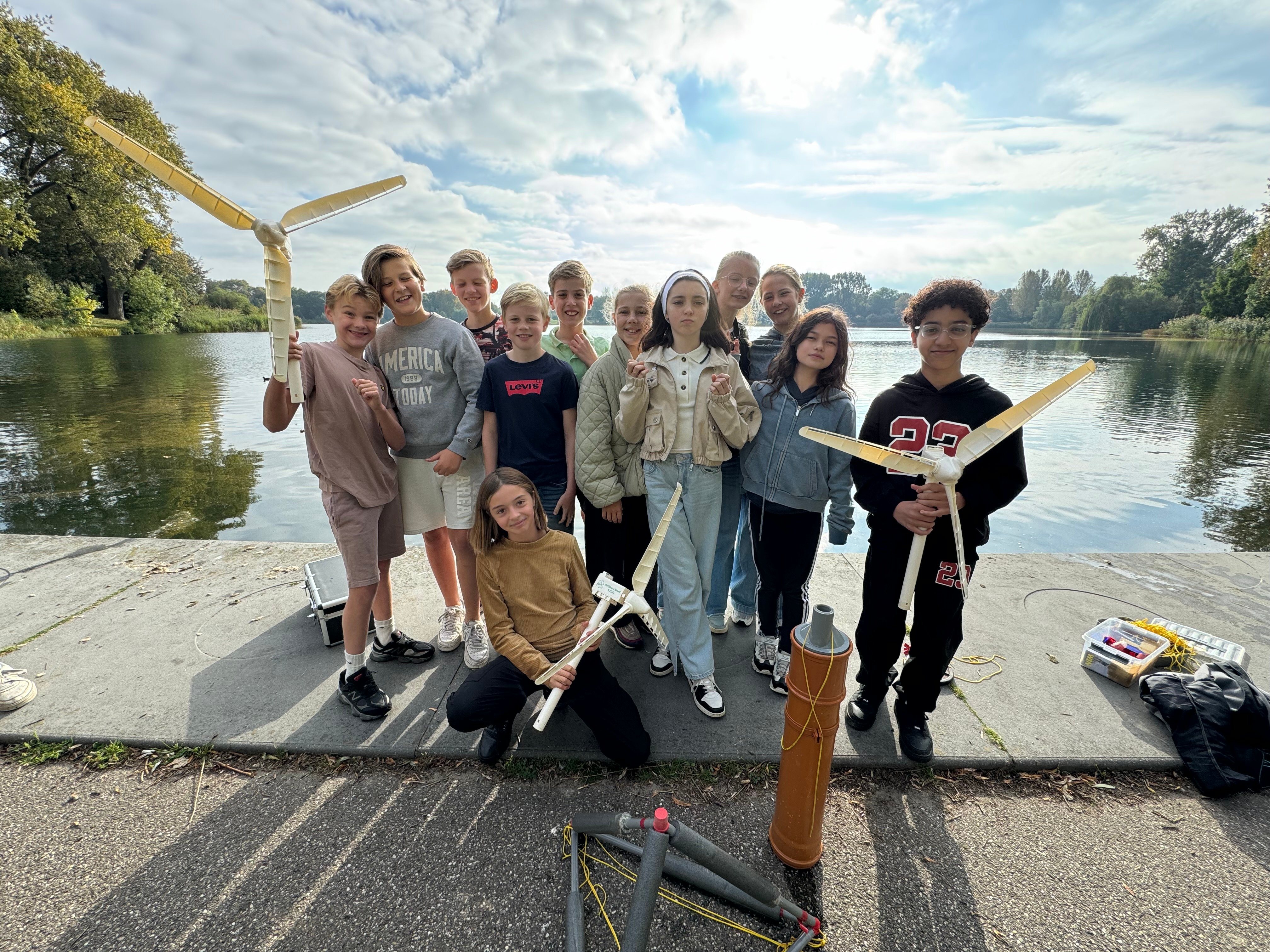 Brunel Foundation Offshore4kids sustainability workshop. Group of students holding wind turbine models near a lake during a Brunel Foundation Offshore4kids sustainability workshop.