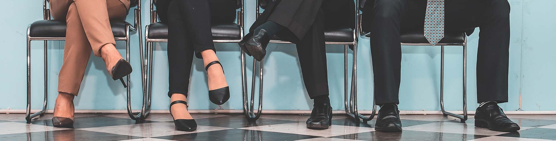 Legs of four people in business attire sitting on a row of chairs