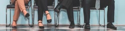 Legs of four people in business attire sitting on a row of chairs