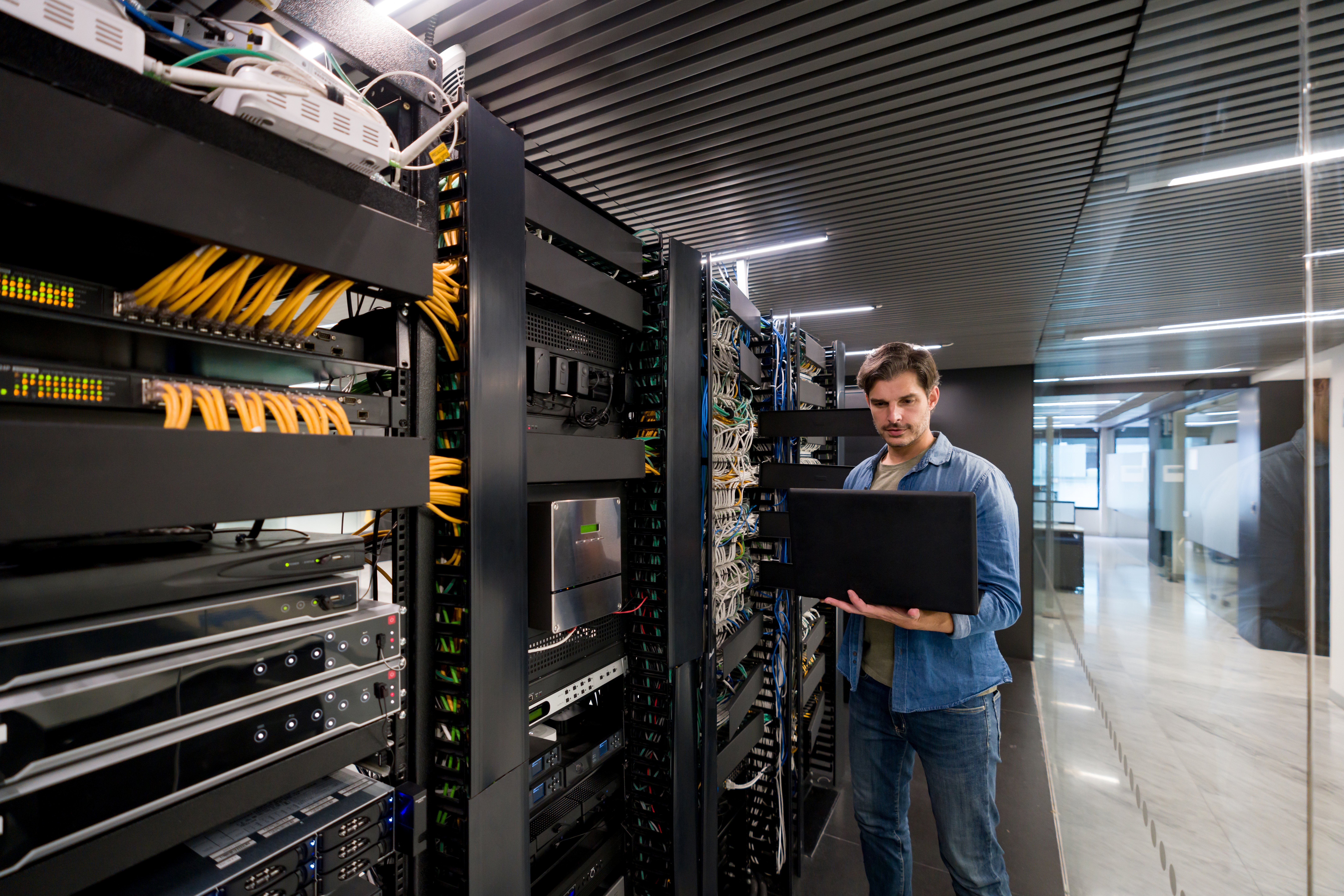 Technician performing maintenance on network racks and cabling inside a modern data center.