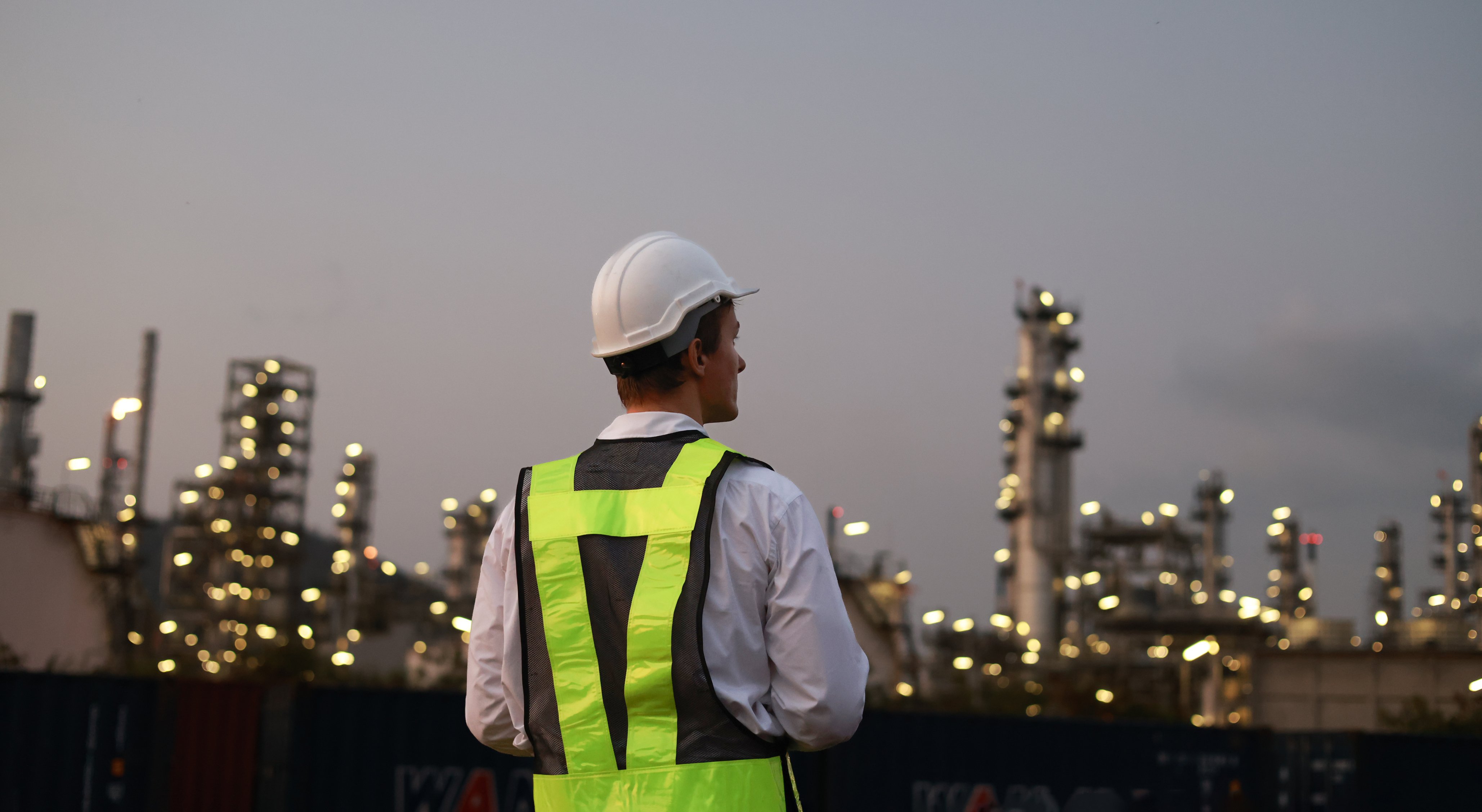 Safety supervisor surveying illuminated refinery at dusk, leadership responsibilities in oil rig jobs