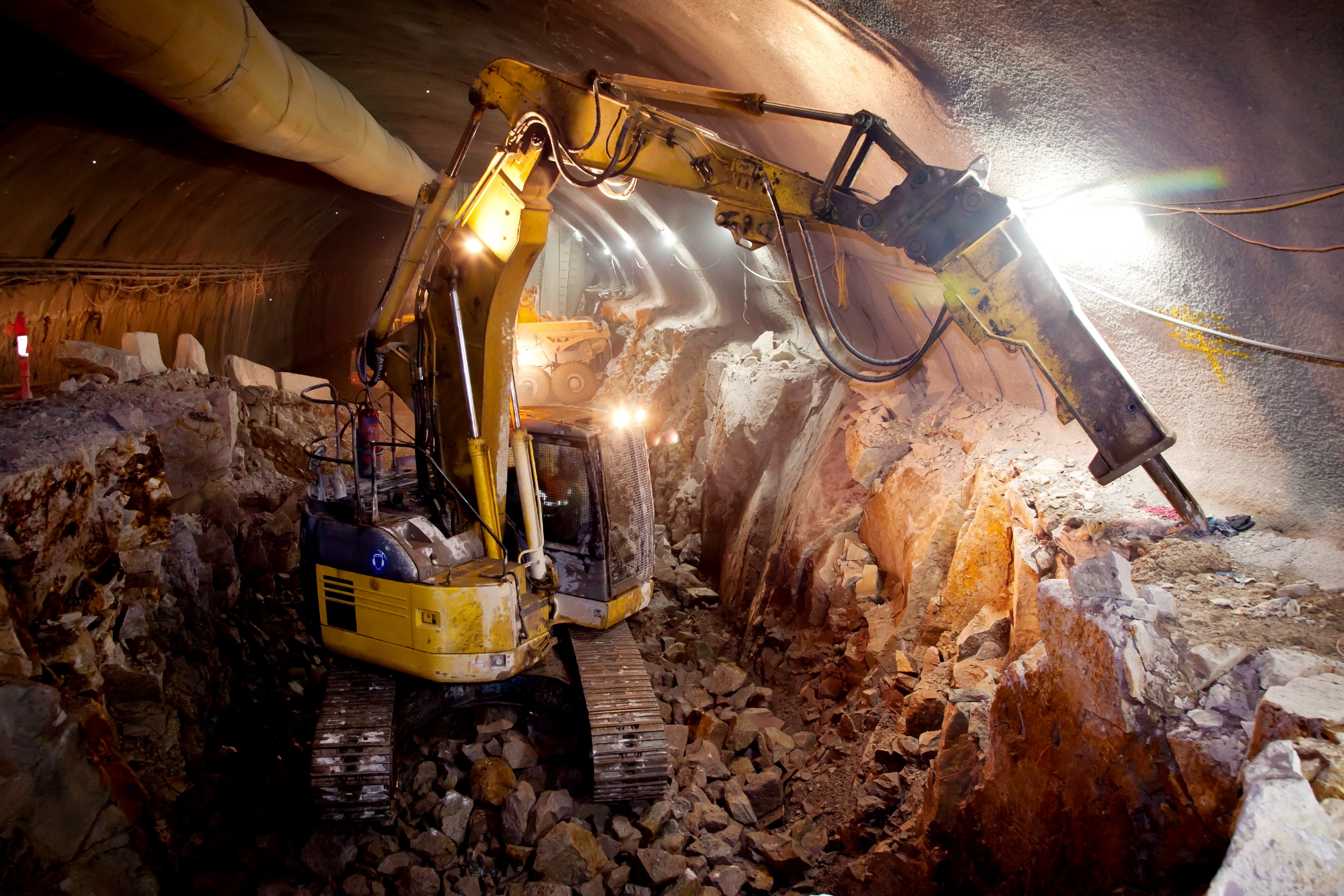 block caving subsurface mining operation with excavator removing broken ore in underground tunnel