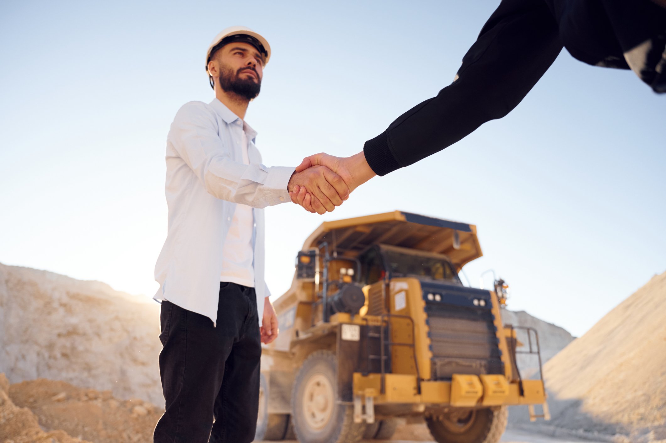 Worker at mine smiles as a mining recruitment support professional shakes their hand in front of a mining truck