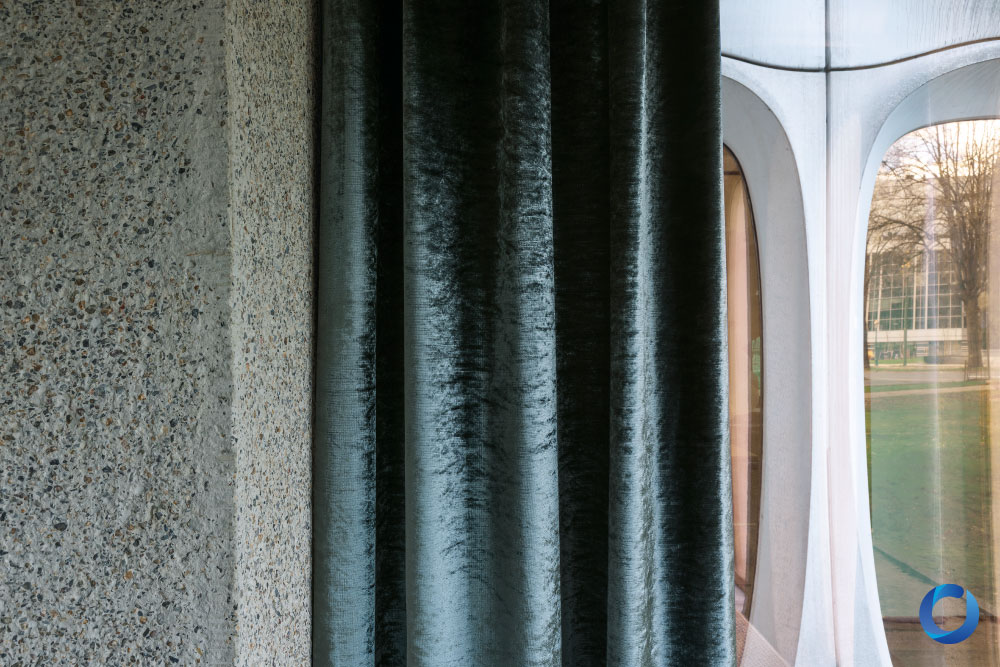 Velvet dark green curtains beside textured stone wall. Collection Osiris