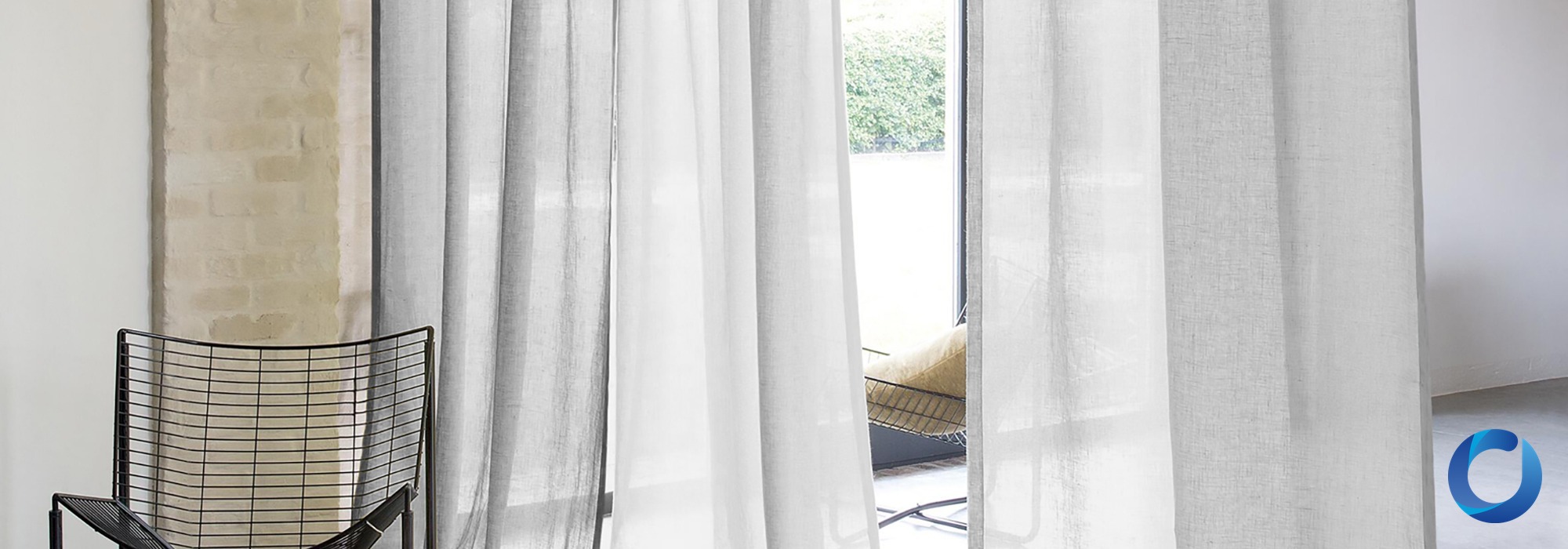Sheer white linen curtains framing a garden view beside a rendered brick pillar and black wire-frame chair, James Dunlop Coastal collection