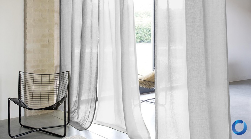 Sheer white linen curtains framing a garden view beside a rendered brick pillar and black wire-frame chair, James Dunlop Coastal collection