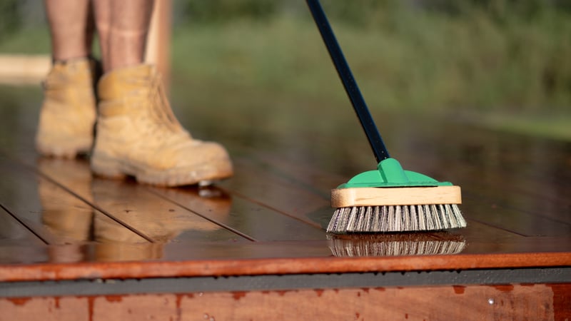 A brush is evenly applying stain to the deck