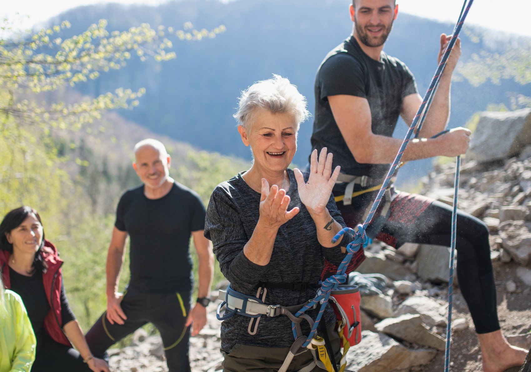 Group of seniors with instructor using chalk before climbing rocks outdoors in nature active lifestyle
