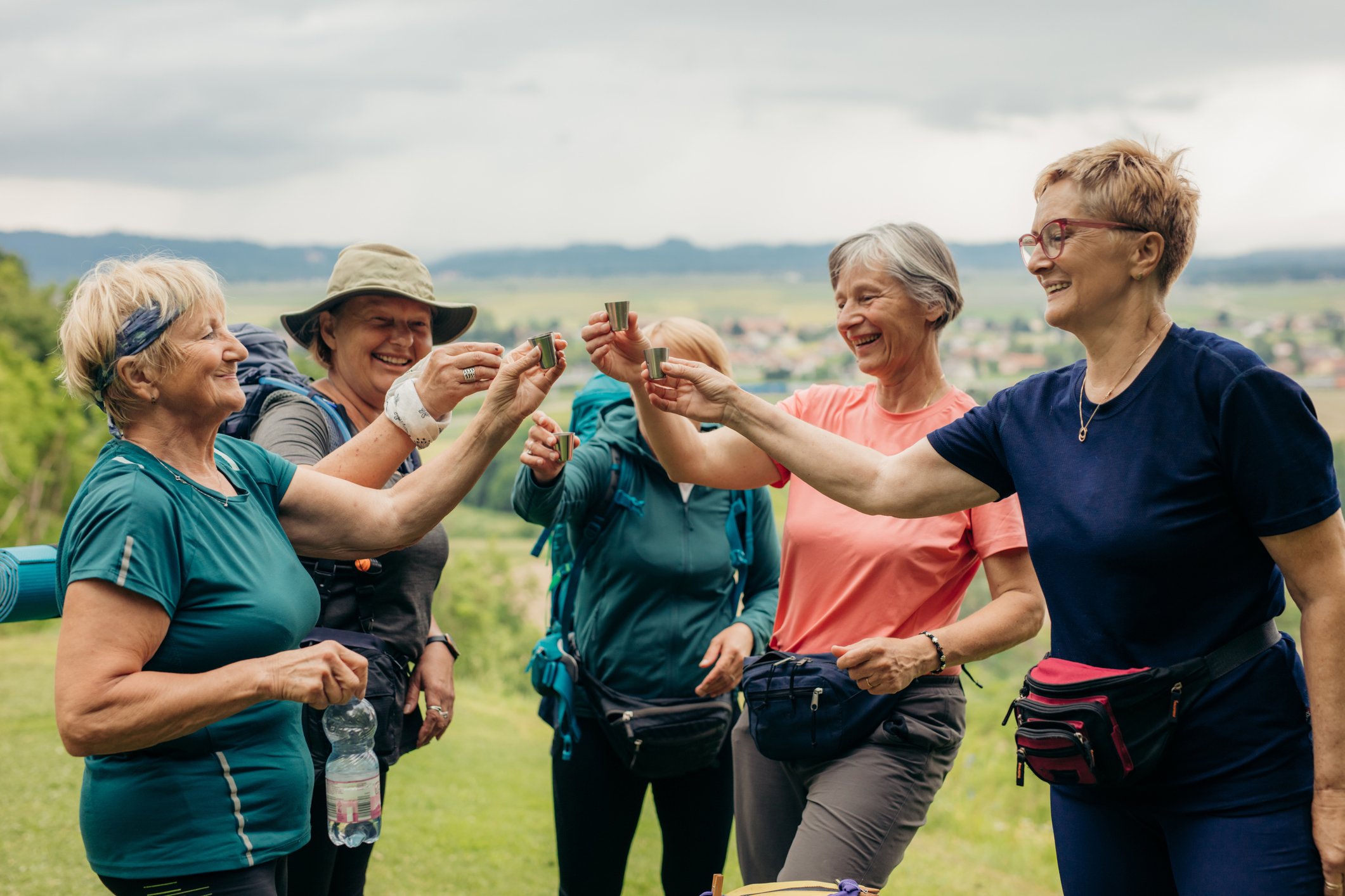 Smiling mature female hikers toasting with shots
