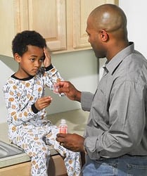 Child taking medicine with father's help