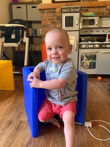 child by blue chair with trach vent