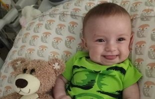 Infant Claire smiling next to a bear plush toy