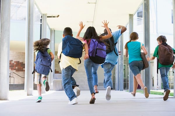 Kids wearing backpacks run down a school hallway.
